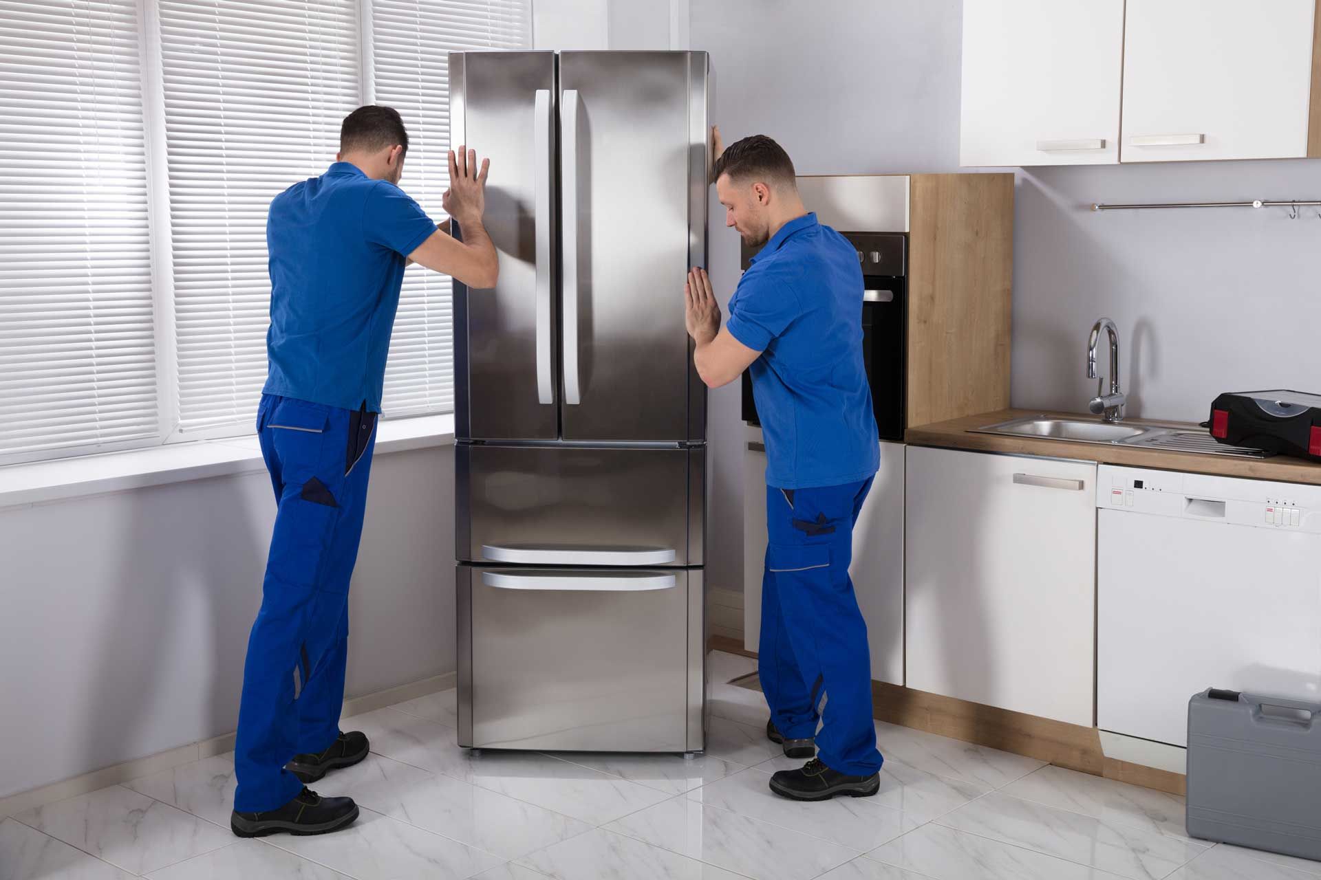 Two men are installing a stainless steel refrigerator in a kitchen.