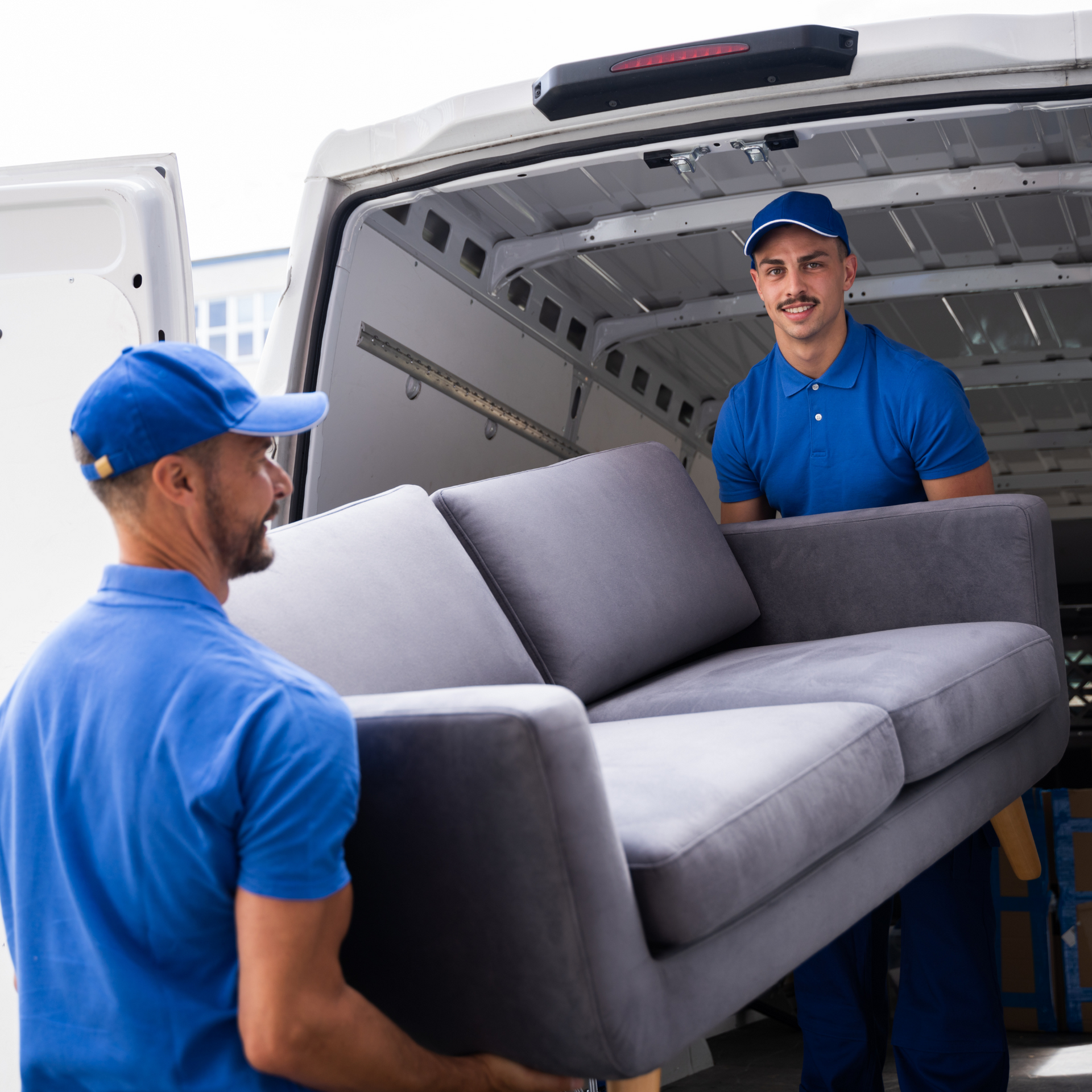 Two men are carrying a couch out of a van.