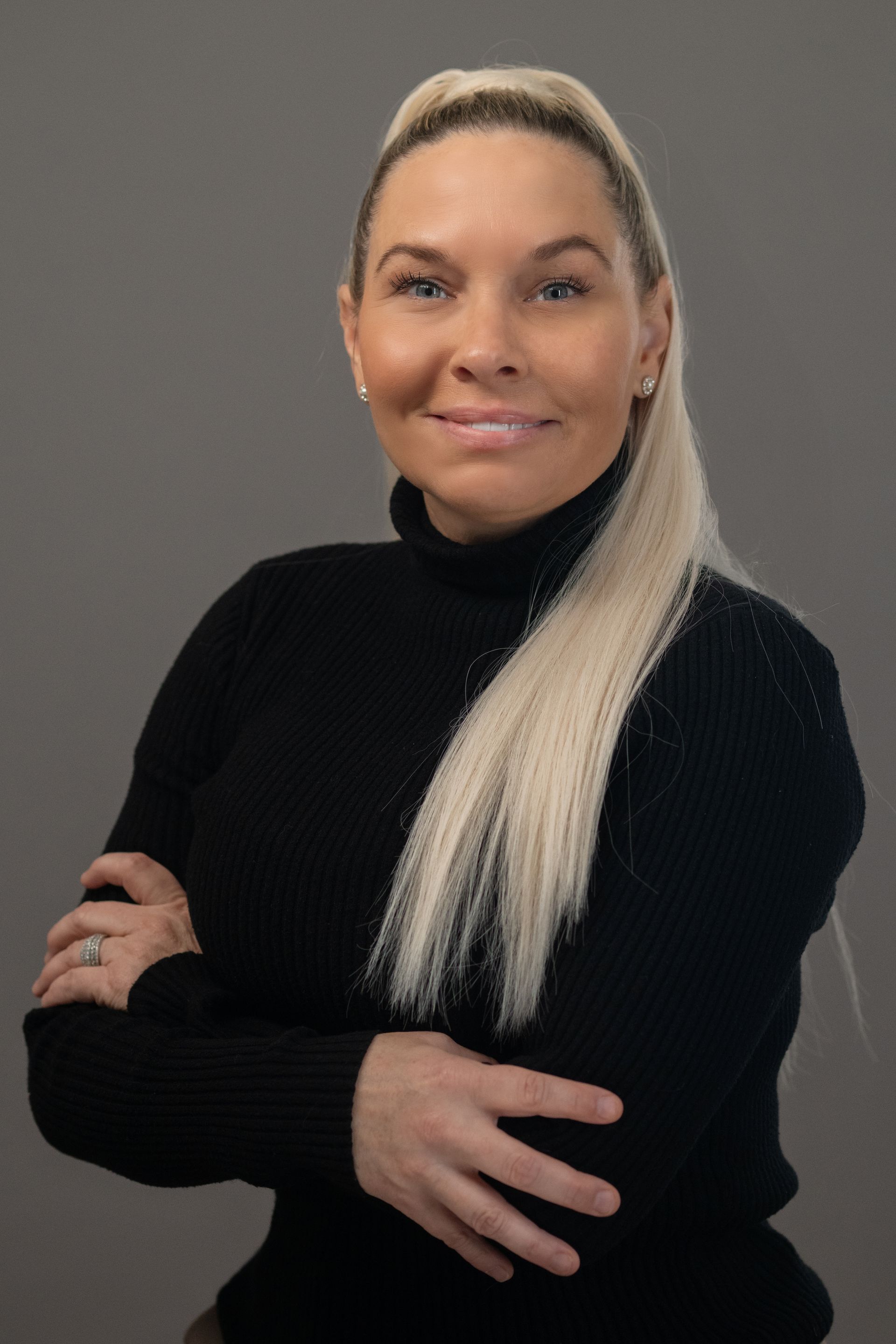 Woman with blonde hair wearing a black turtleneck, arms crossed, smiling.