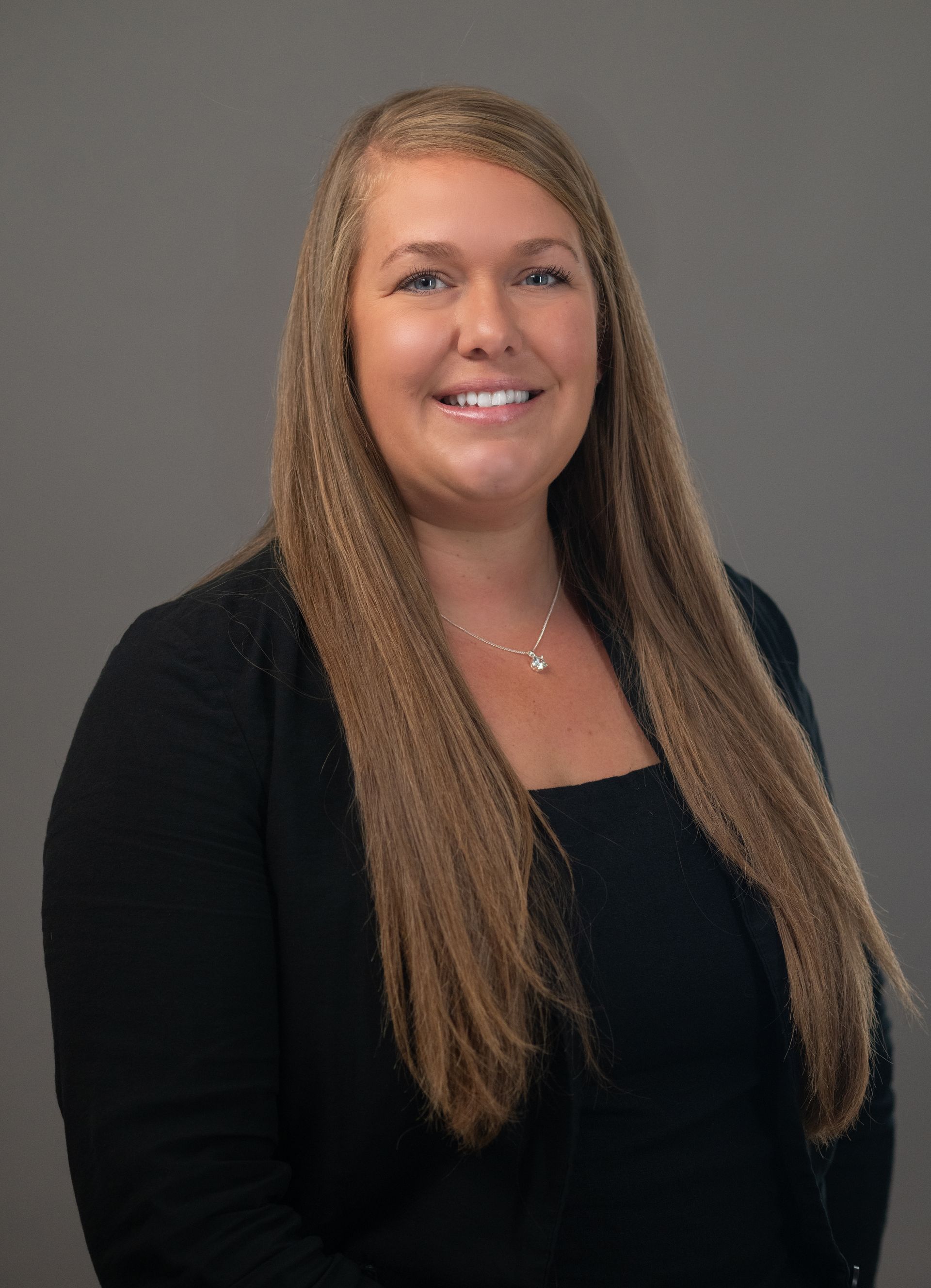 Man with a beard and a teal polo shirt smiling, arms crossed, grey background.
