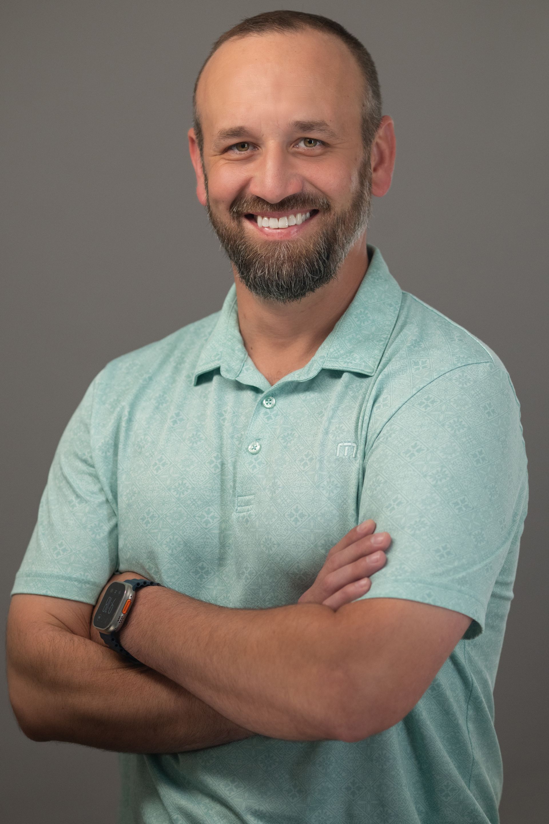 Woman wearing glasses, pink cardigan, smiling, looking at the camera. Against a gray background.