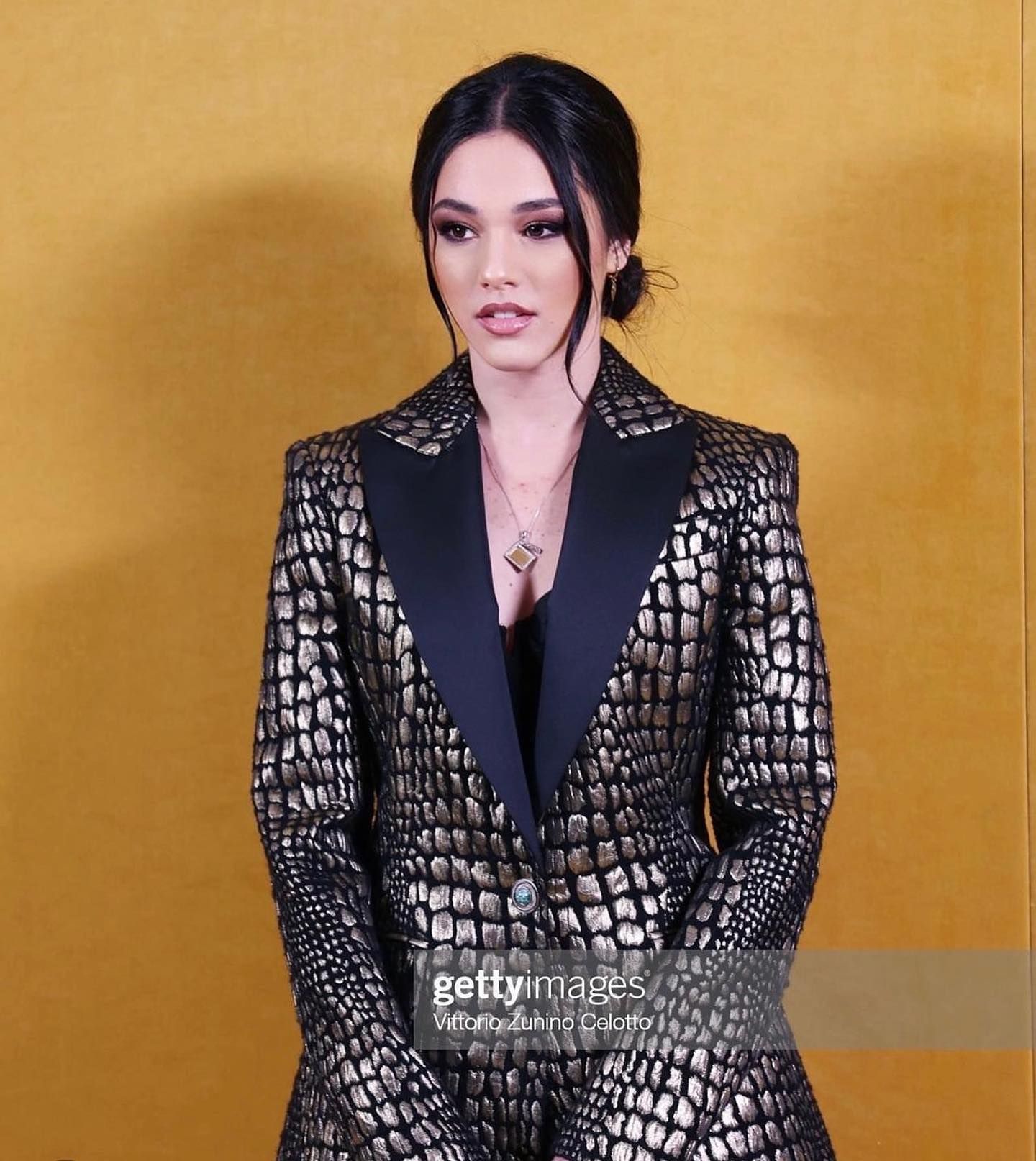 Una donna in un abito nero e oro è in piedi davanti a un muro giallo.