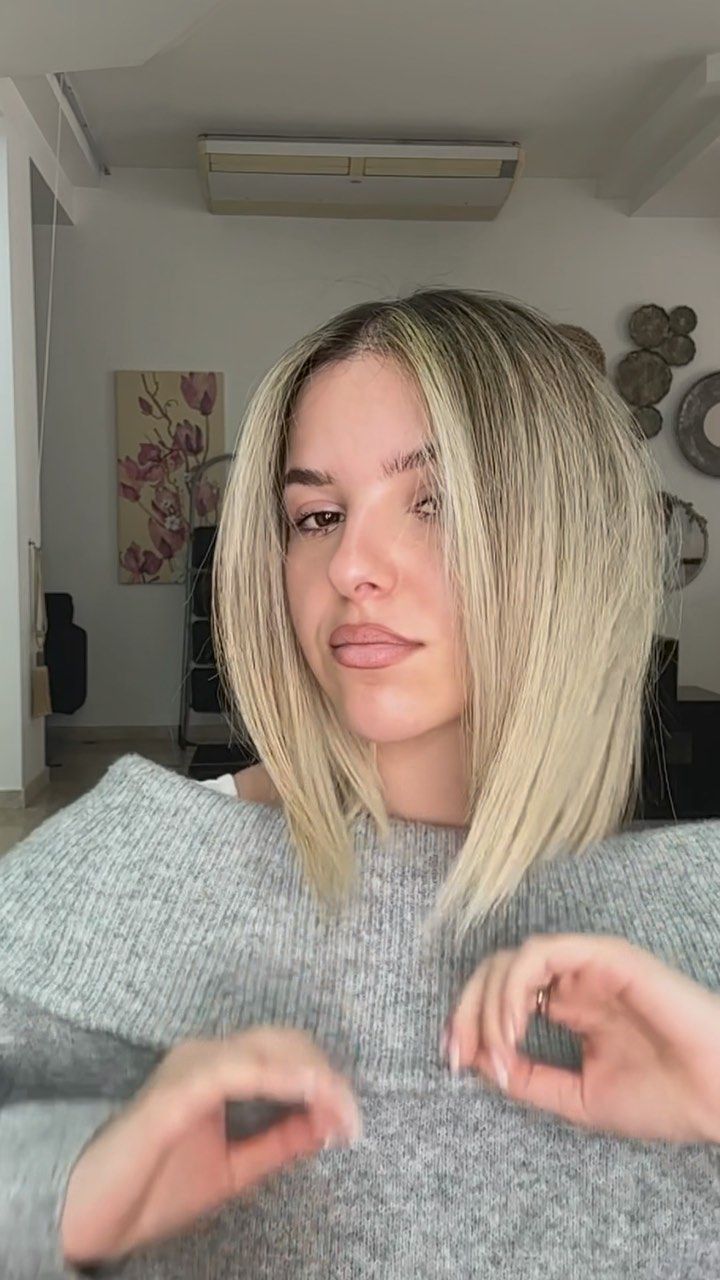 Una donna con i capelli biondi indossa un maglione grigio.