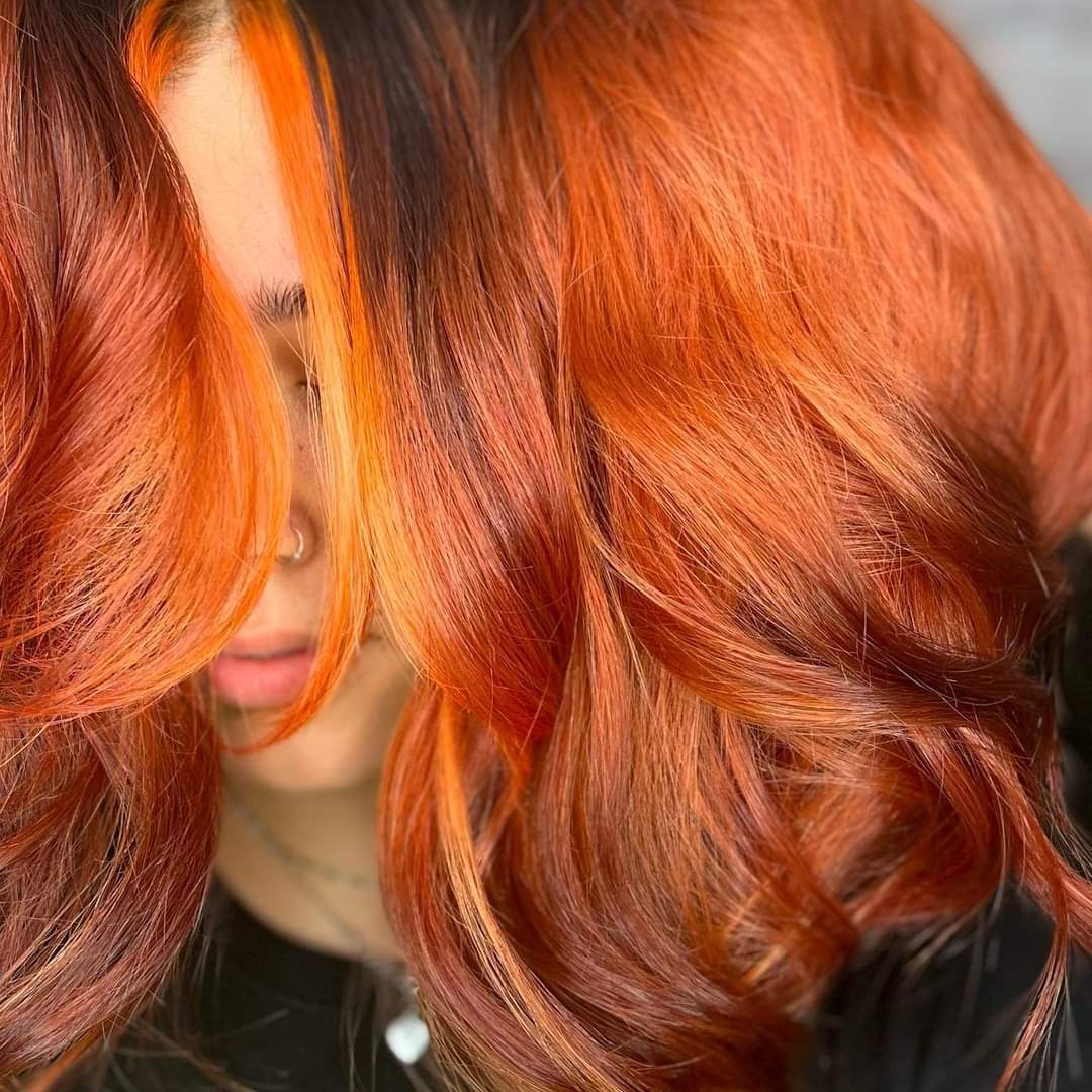 Una donna con lunghi capelli rossi si copre il viso con i capelli.