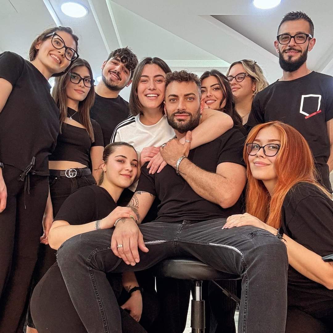 Un gruppo di persone posa per una foto con un uomo seduto su uno sgabello.