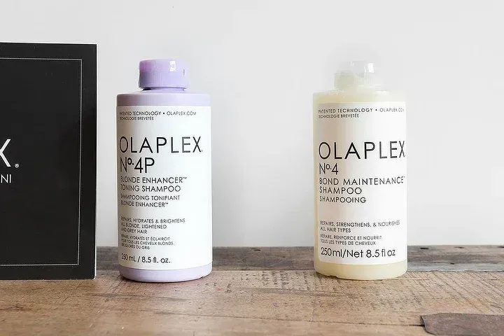Due flaconi di prodotti per capelli Olaplex sono appoggiati su un tavolo di legno.