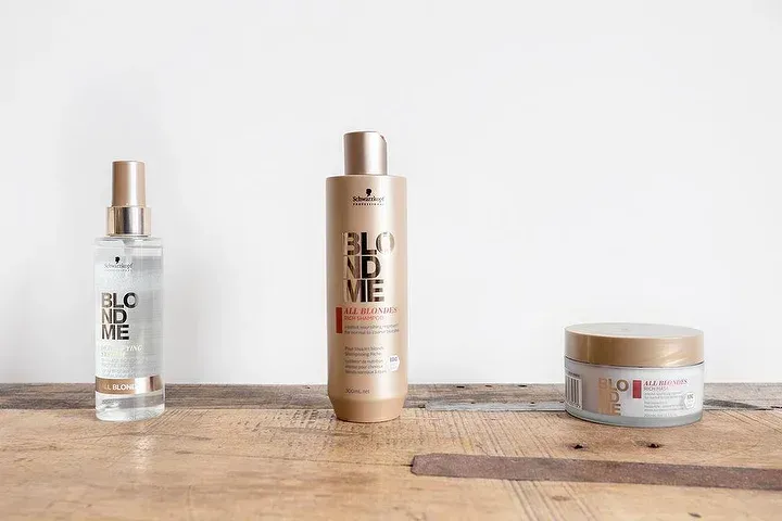 Tre flaconi di prodotti per capelli sono appoggiati su un tavolo di legno.