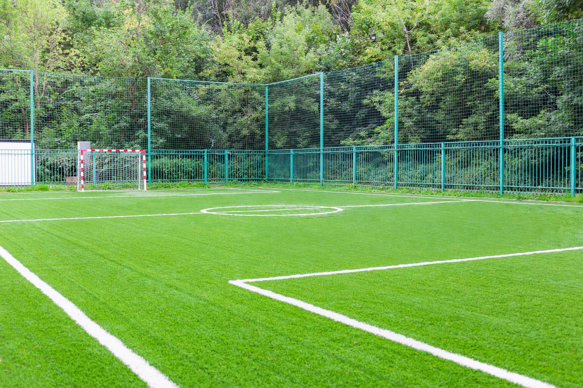 Un campo da calcio all'aperto con manto erboso artificiale di un verde brillante, linee di confine bianche e una porta, circondato da una recinzione.
