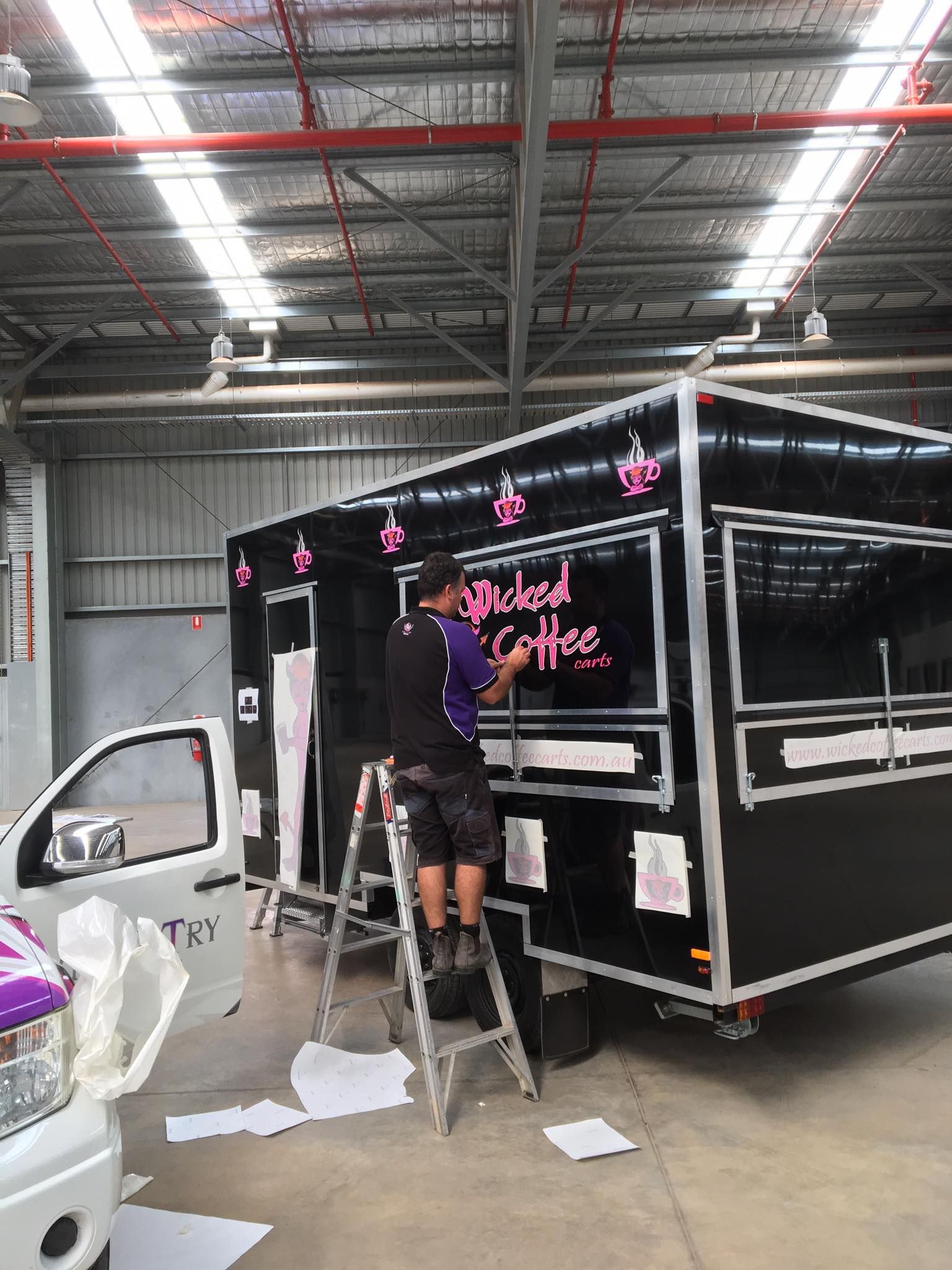 A man is standing on a ladder in front of a food truck.