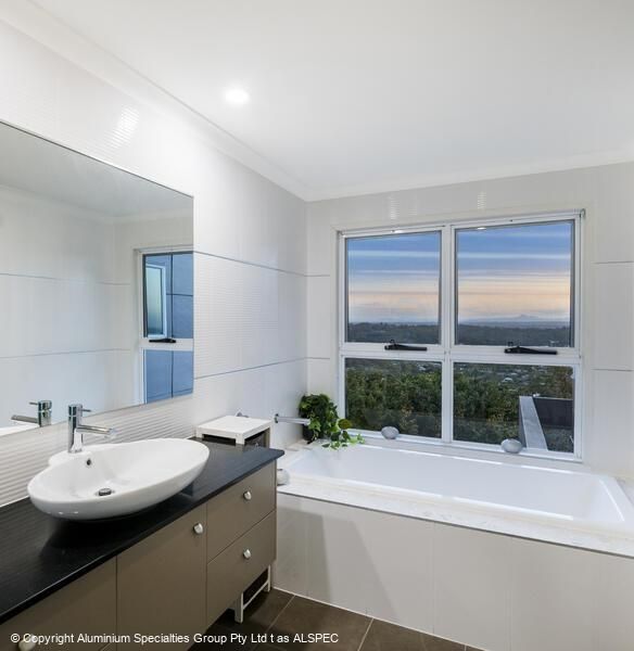Bathroom with a white bathtub, vanity, and window overlooking a natural landscape.