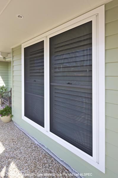 Two rectangular windows with dark screens and white frames on a light green wall.