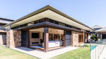 Modern home with stone walls, open sliding doors, and a flat roof, next to a pool.