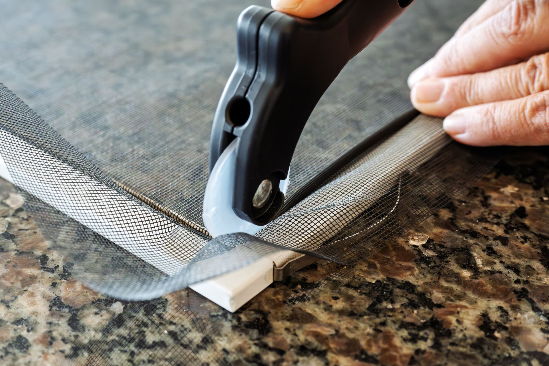 Close-up of a worker rescreening the mesh of a window screen with a spline roller tool