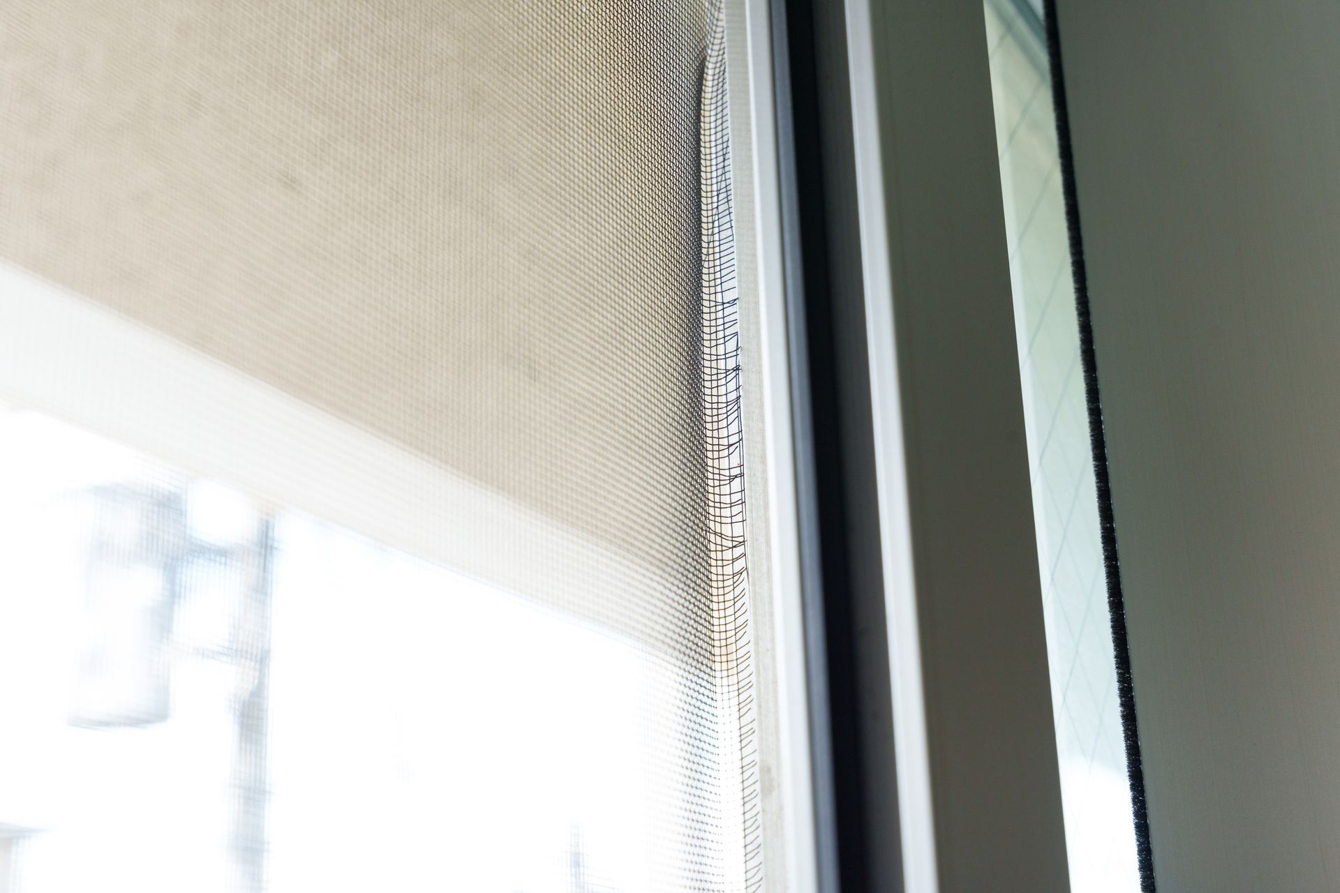 A close-up of a mesh security screen window broken on the edges.