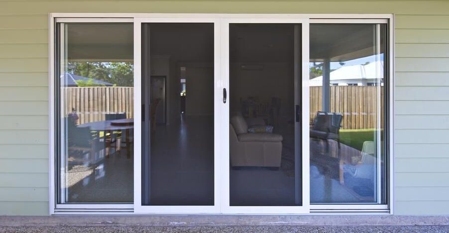 Sliding glass door with screen, white frame. View of interior living space and exterior patio.