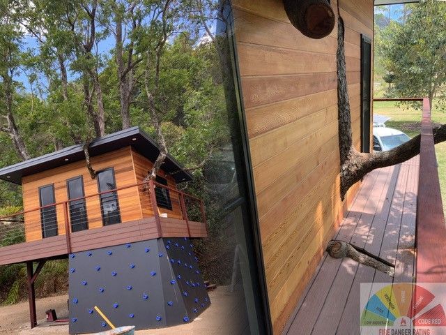 Wooden treehouse with climbing wall, integrated into a tree in a forest setting.