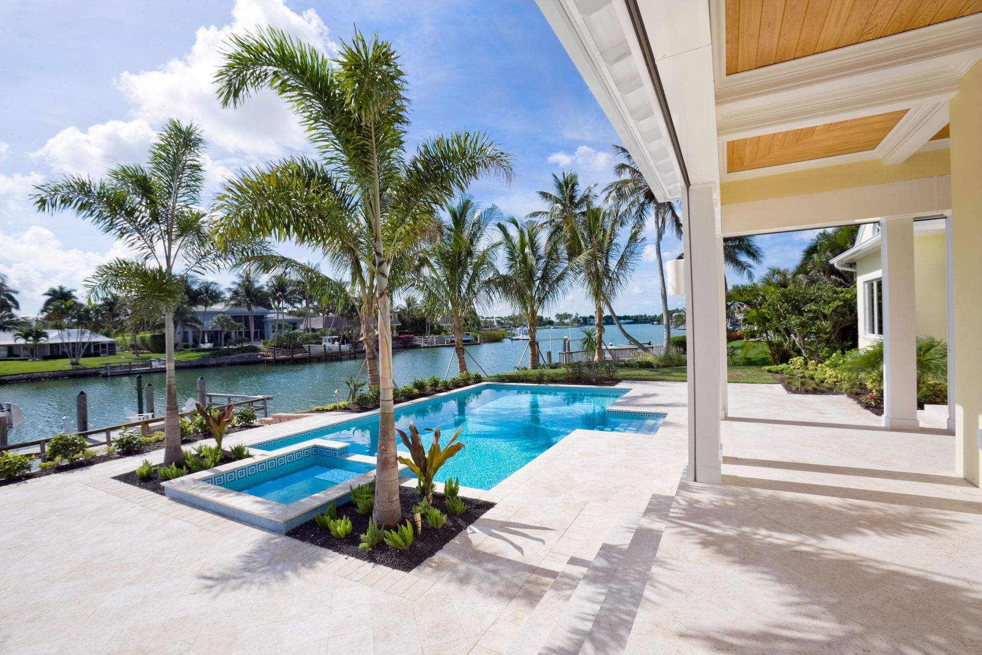 Home with enclosed patio, lawn, poolside lounge chairs and umbrella, and lush palm grove.