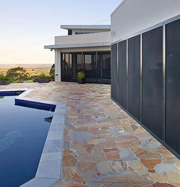 Patio with pool, flagstone pavers, and modern house. Black screens line the building's side, overlooking a landscape.