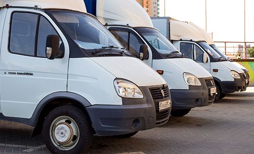 A row of white vans are parked in a parking lot.