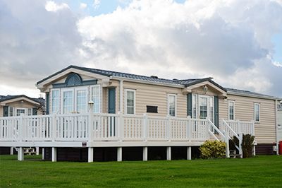 A mobile home with a large deck is sitting on top of a lush green field.