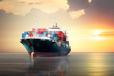 A large container ship is floating on top of a body of water at sunset.