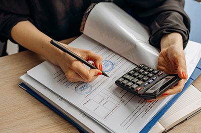 A woman is holding a calculator and writing on a piece of paper.