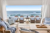 Beachfront living room with white sofas, wicker chairs, and an ocean view through open curtains.