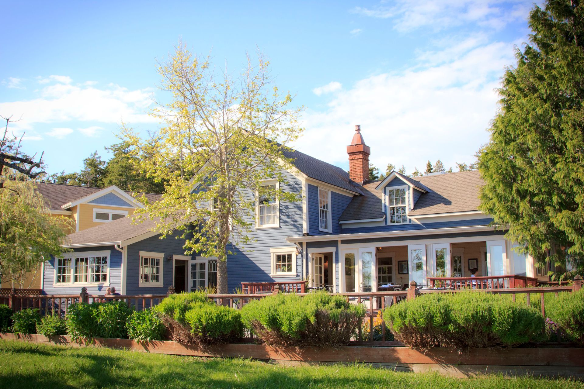 A large blue house with a red chimney is surrounded by trees and bushes.