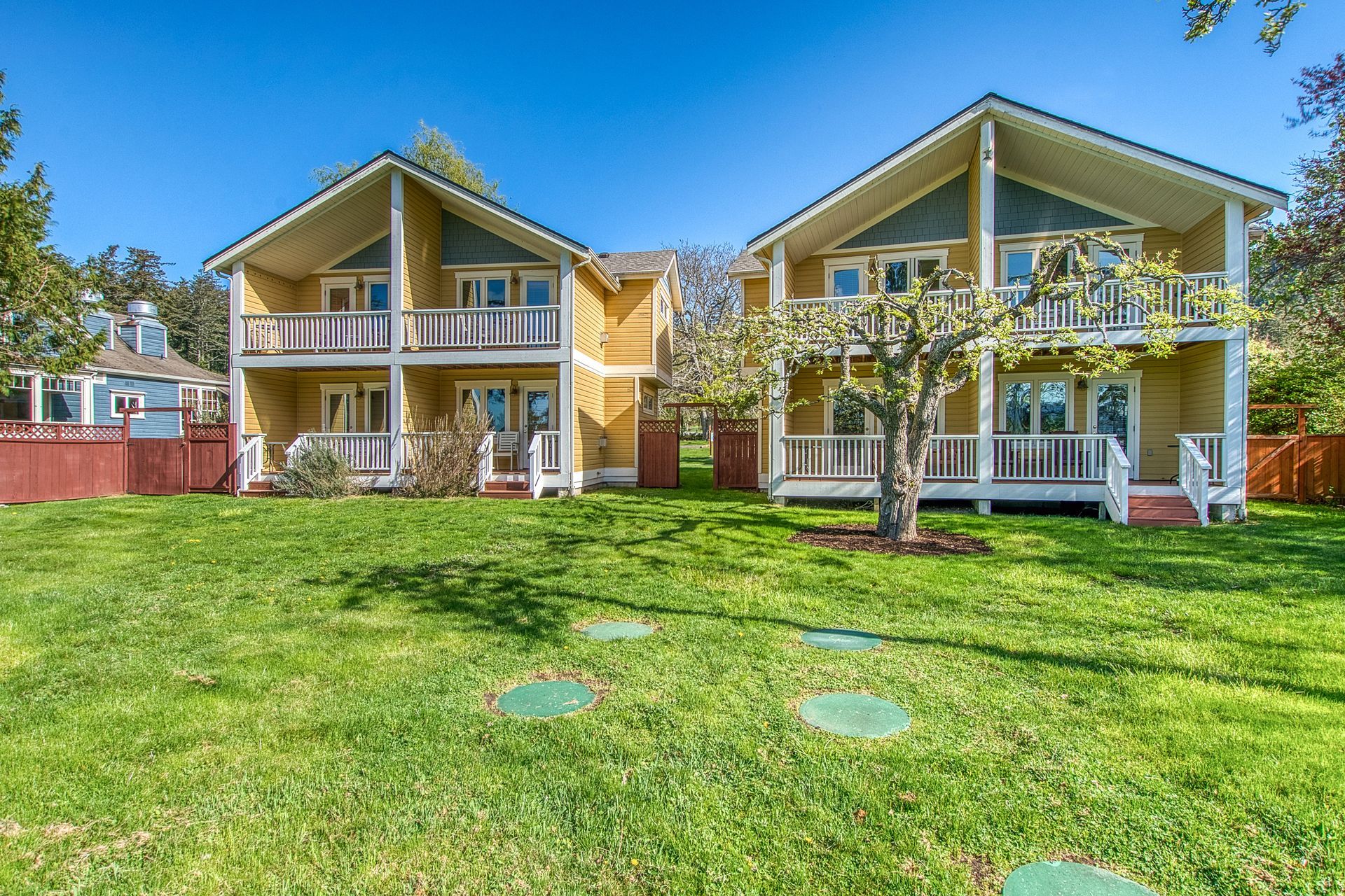 A yellow house with a white porch and stairs is in the middle of a grassy field.