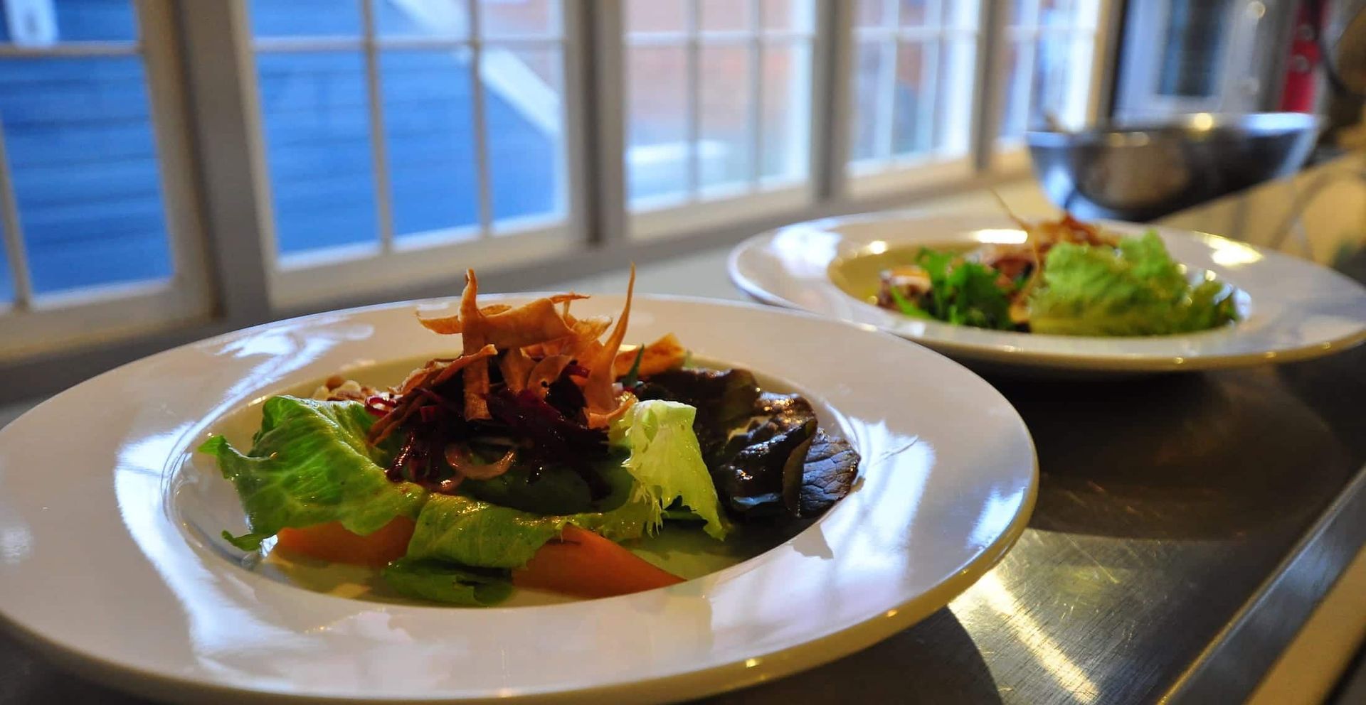 Two plates of food are sitting on a table in front of a window.