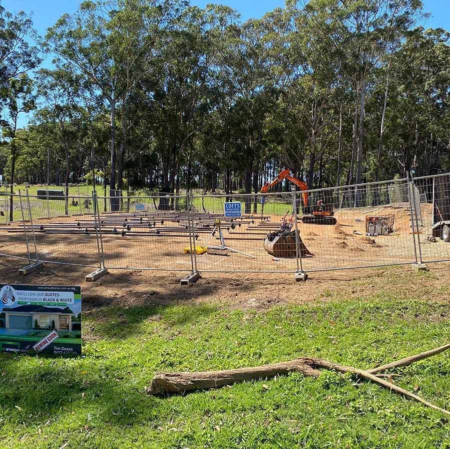 A Construction Site With A Fence And A Sign In The Grass — Coffs Temporary Fencing Pty Ltd In Sawtell, NSW