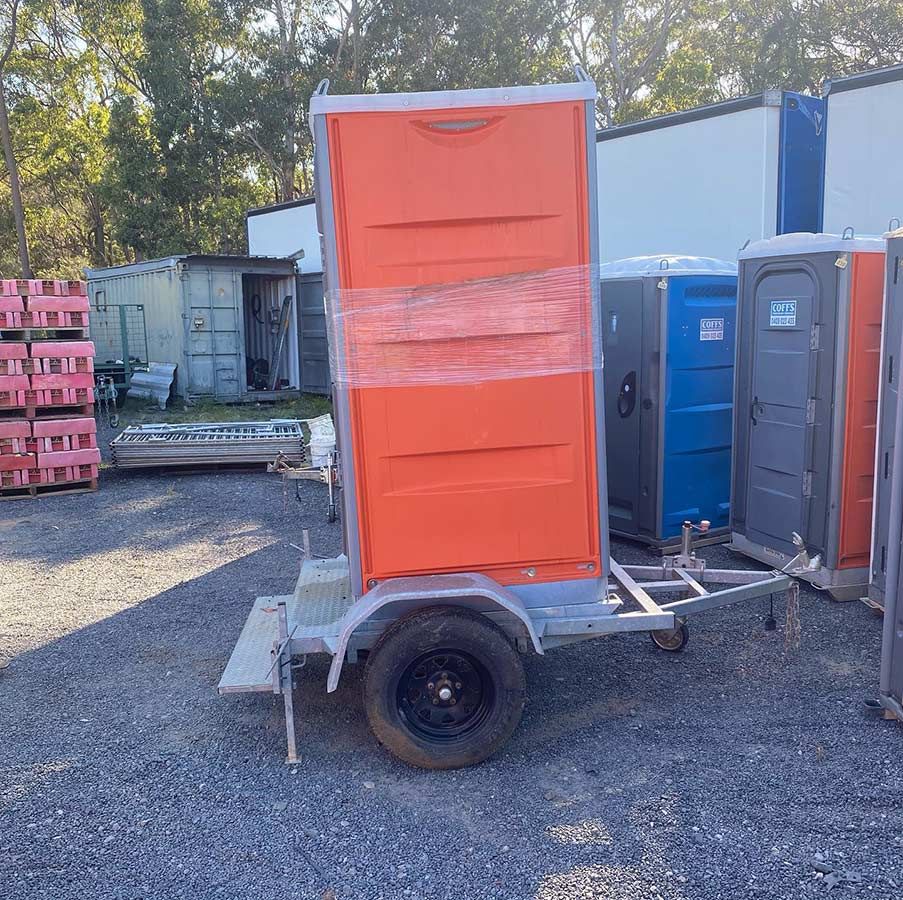 A Trailer With A Toilet On It Is Parked In A Gravel Lot — Coffs Temporary Fencing Pty Ltd In Sawtell, NSW
