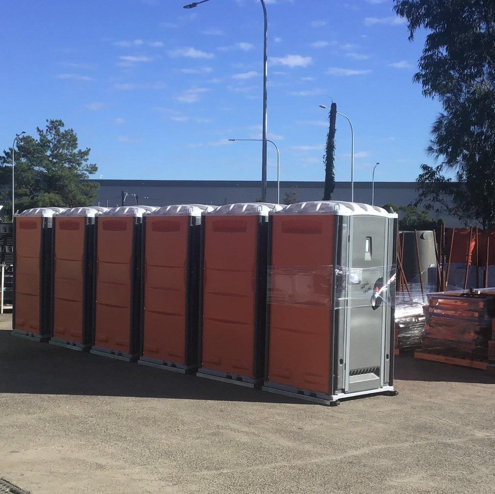 A Row Of Orange Portable Toilets Are Lined Up In A Parking Lot — Coffs Temporary Fencing Pty Ltd In Nambucca Heads, NSW