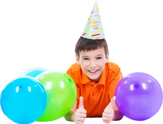 A boy wearing a party hat is laying on the floor with balloons and giving a thumbs up