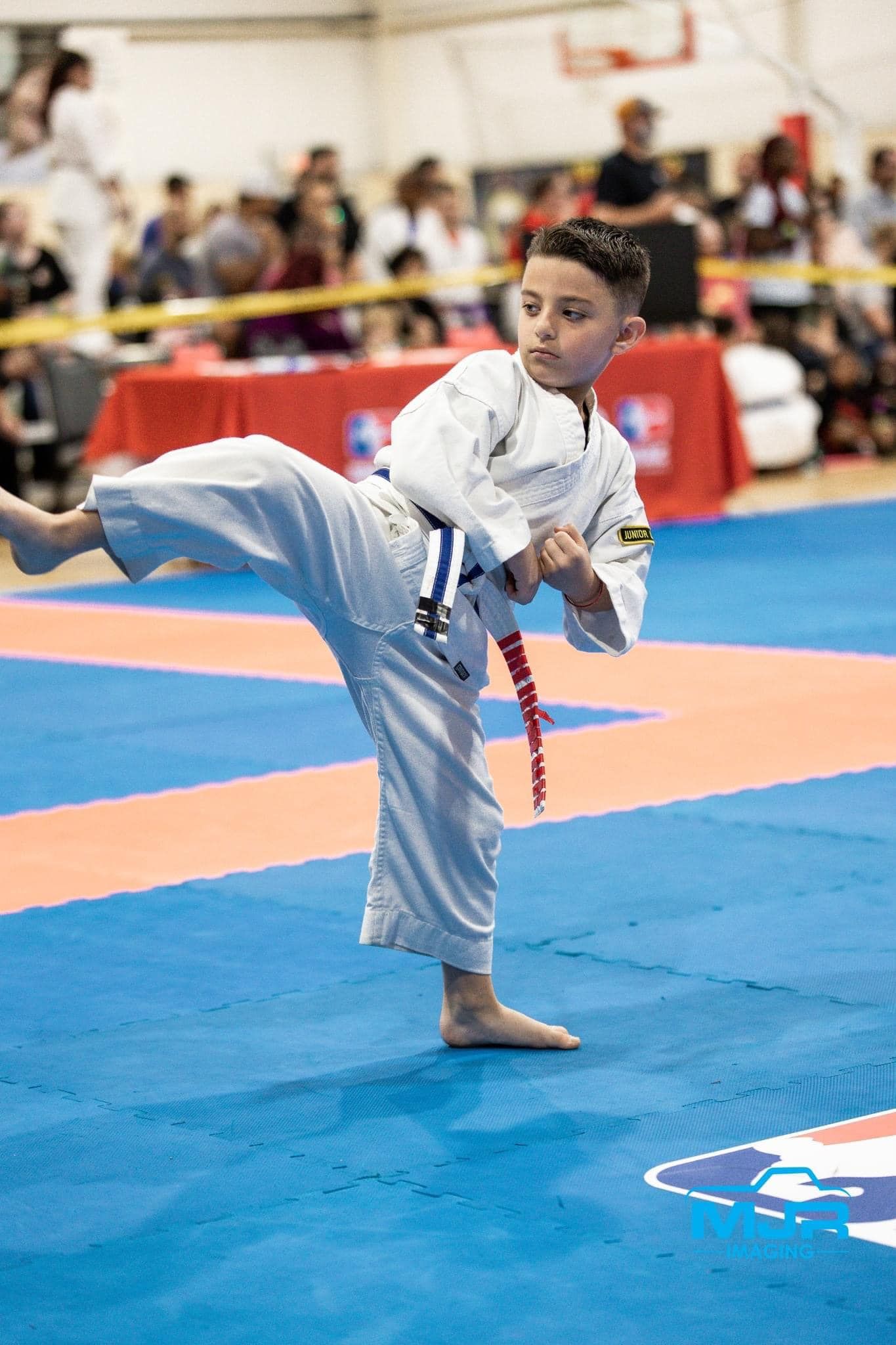 A young boy is practicing karate on a mat in a gym.