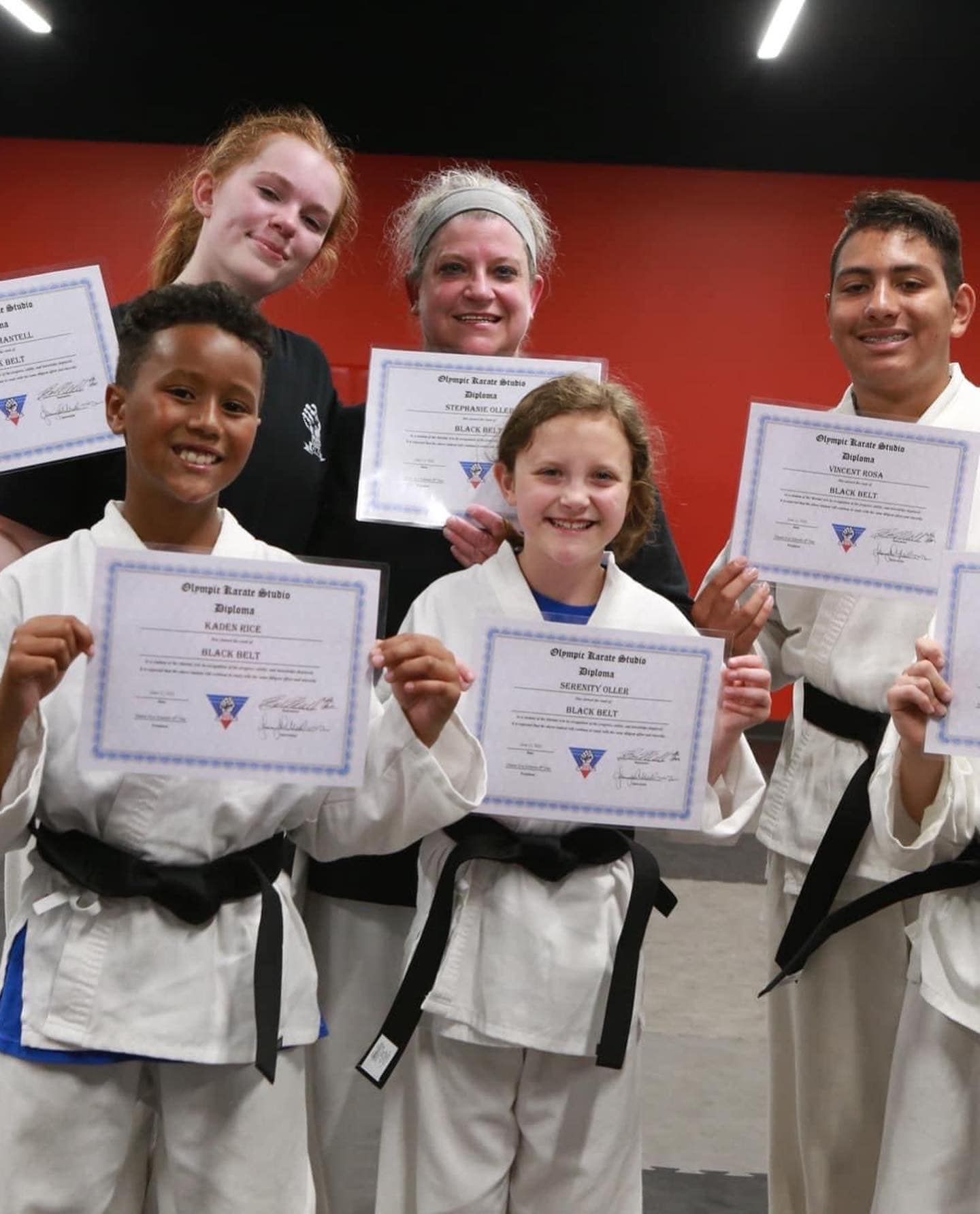 A group of people in karate uniforms are holding up certificates