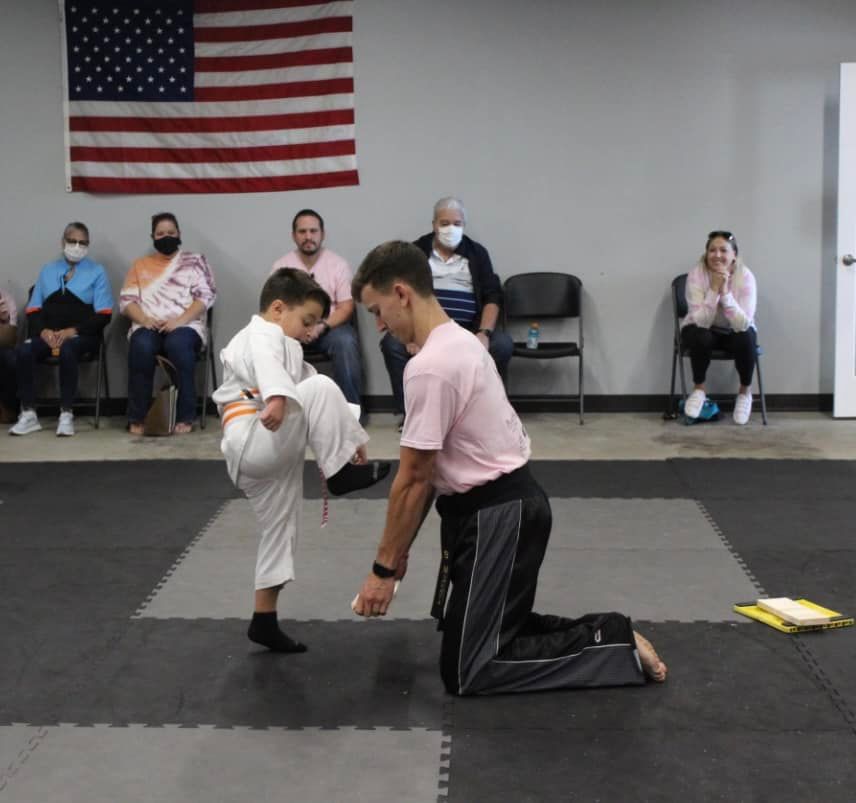 A man in a pink shirt is kneeling next to a young boy in a martial arts class