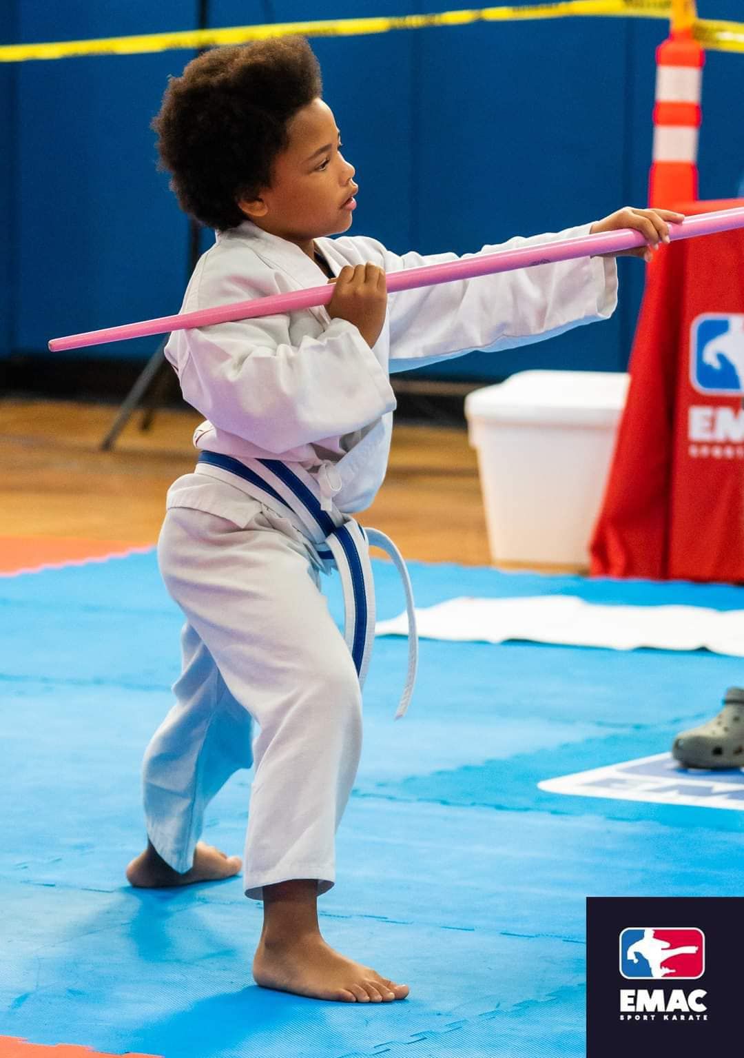 A young boy in a karate uniform is holding a pink stick