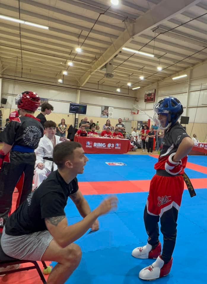 A man is squatting down next to a boy on a karate mat.