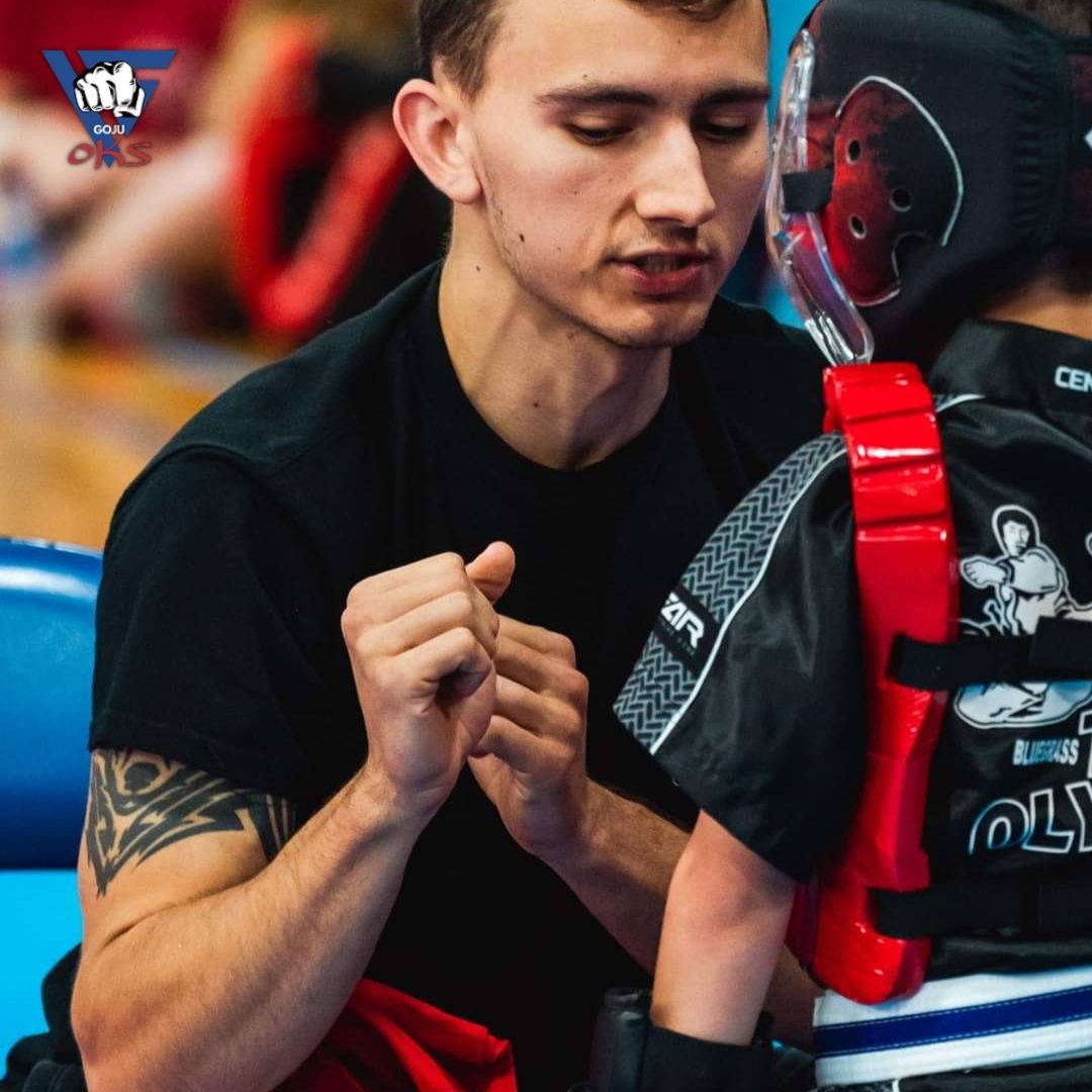A man in a black shirt is talking to a young boy wearing a karate uniform