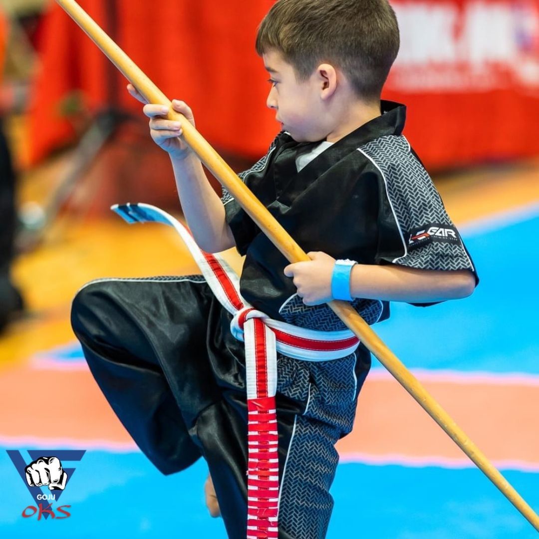 A young boy is holding a wooden stick with a red white and blue belt around his waist
