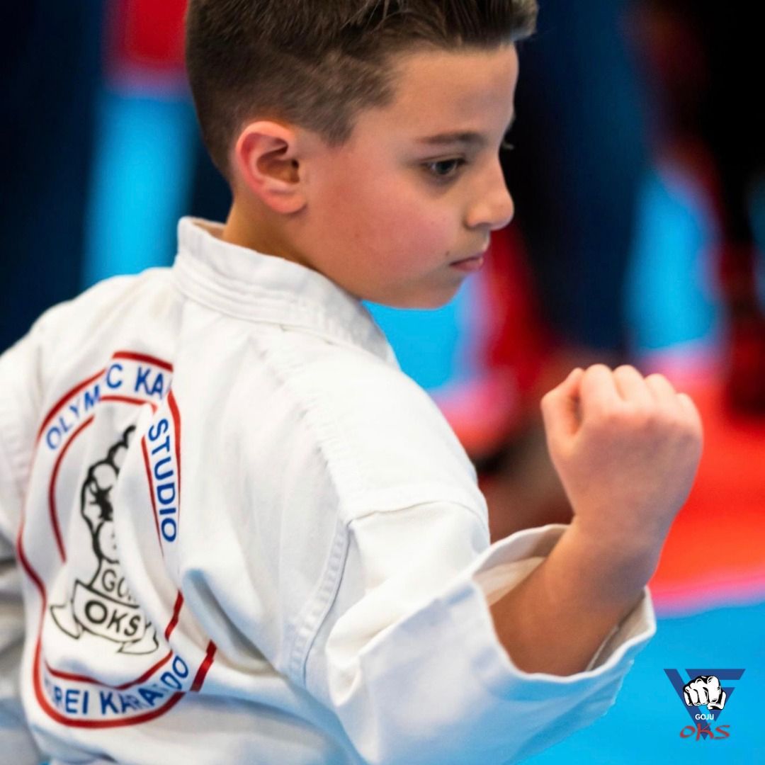 A young boy wearing a white karate uniform with olympic karate studio on the back