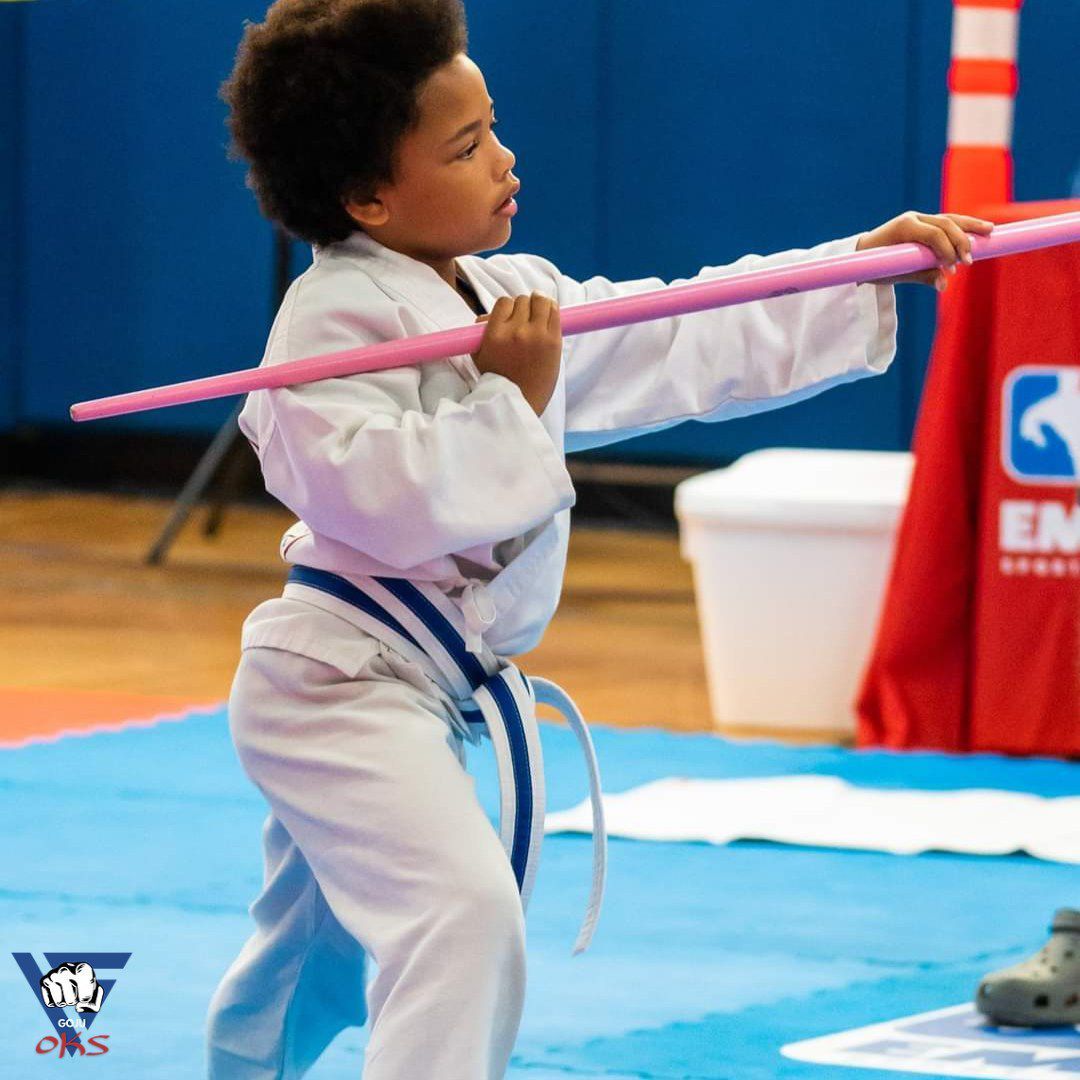 A young boy in a karate uniform is holding a pink stick