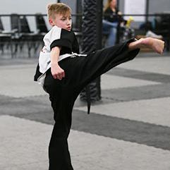 A young boy in a karate uniform is kicking his leg in the air.