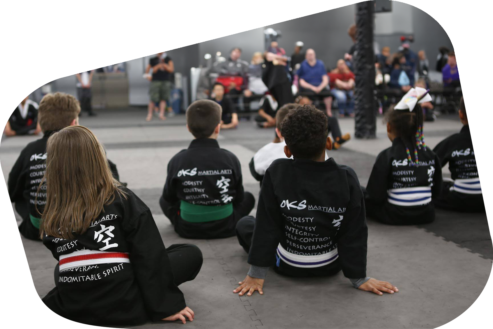 A group of children are sitting on the ground in front of a crowd.