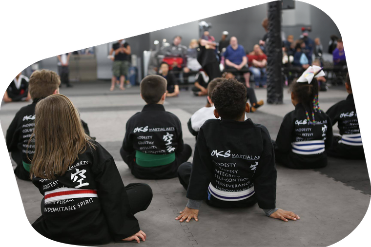 A group of children are sitting on the ground in front of a crowd.