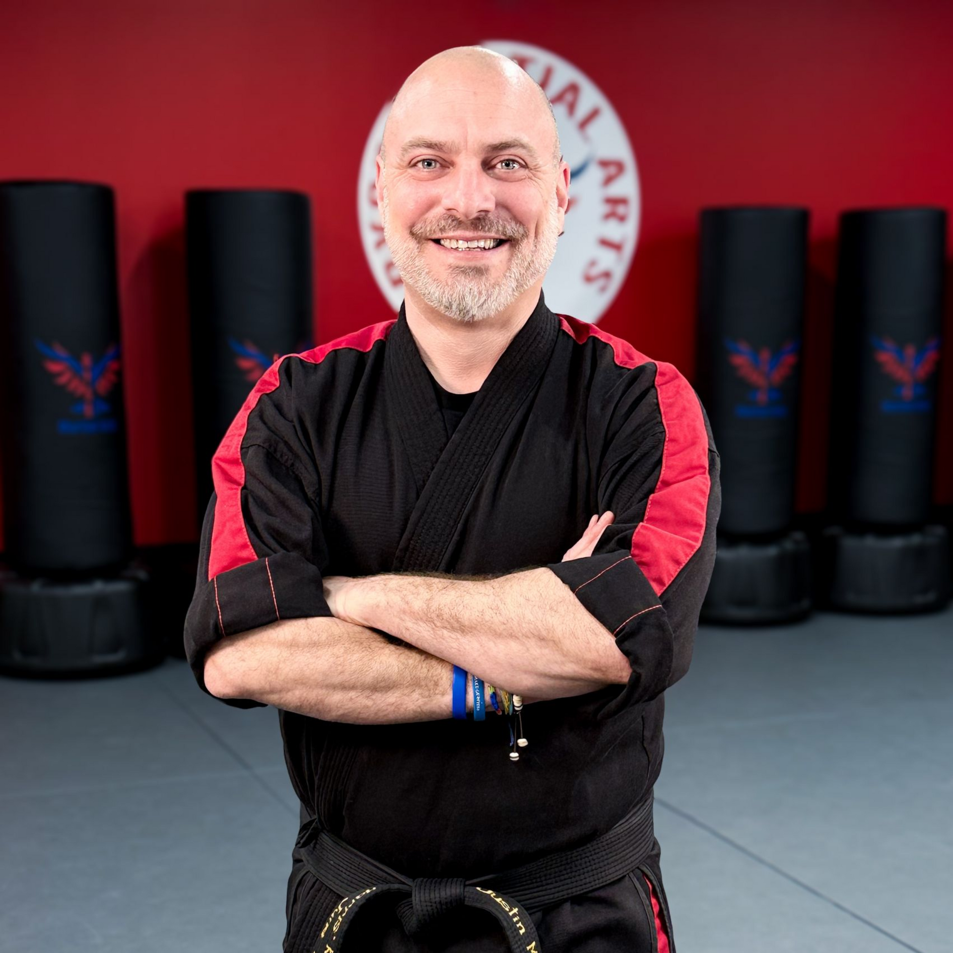 A man in a white karate uniform is standing on a blue mat in a gym.