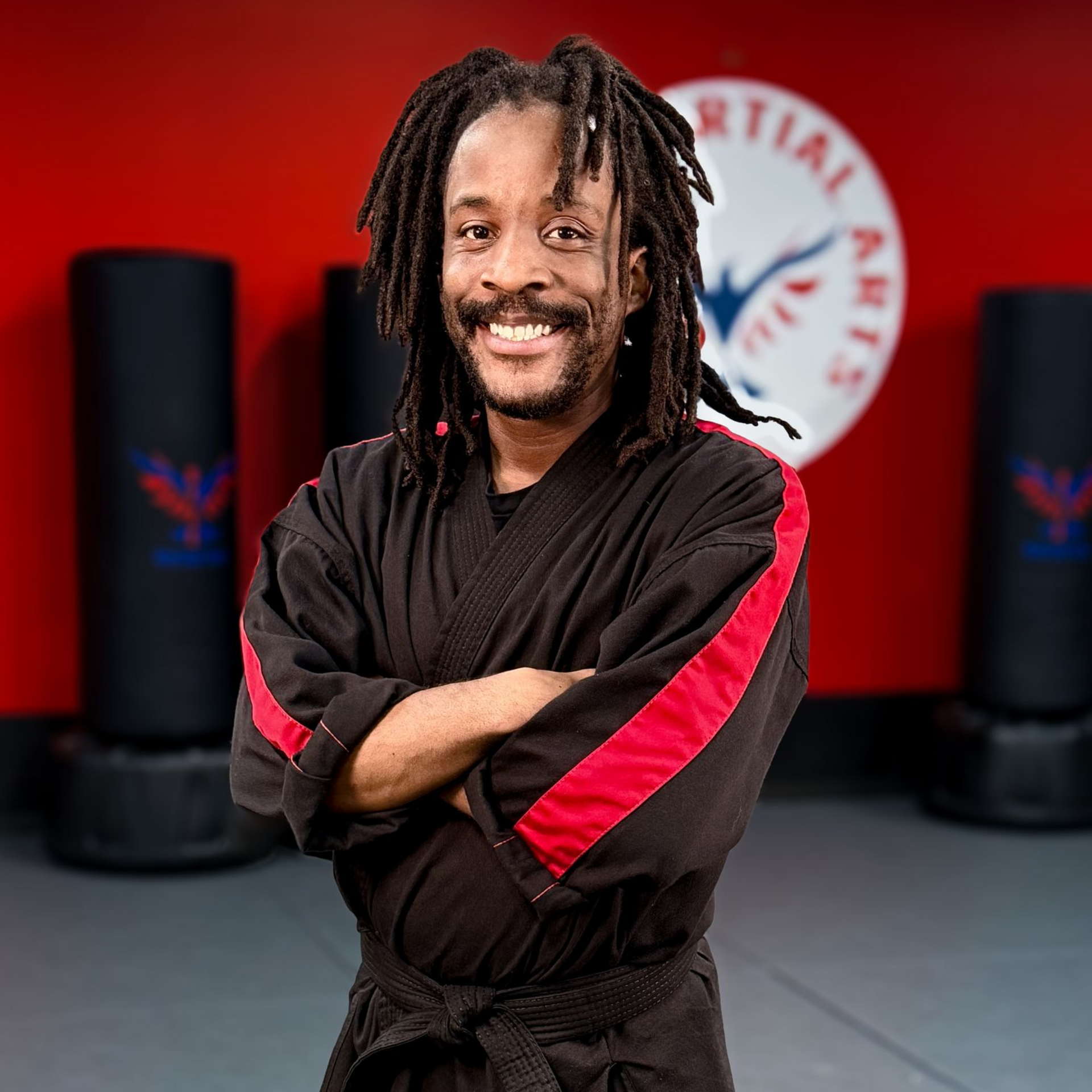 A man in a white karate uniform is standing on a blue mat in a gym.