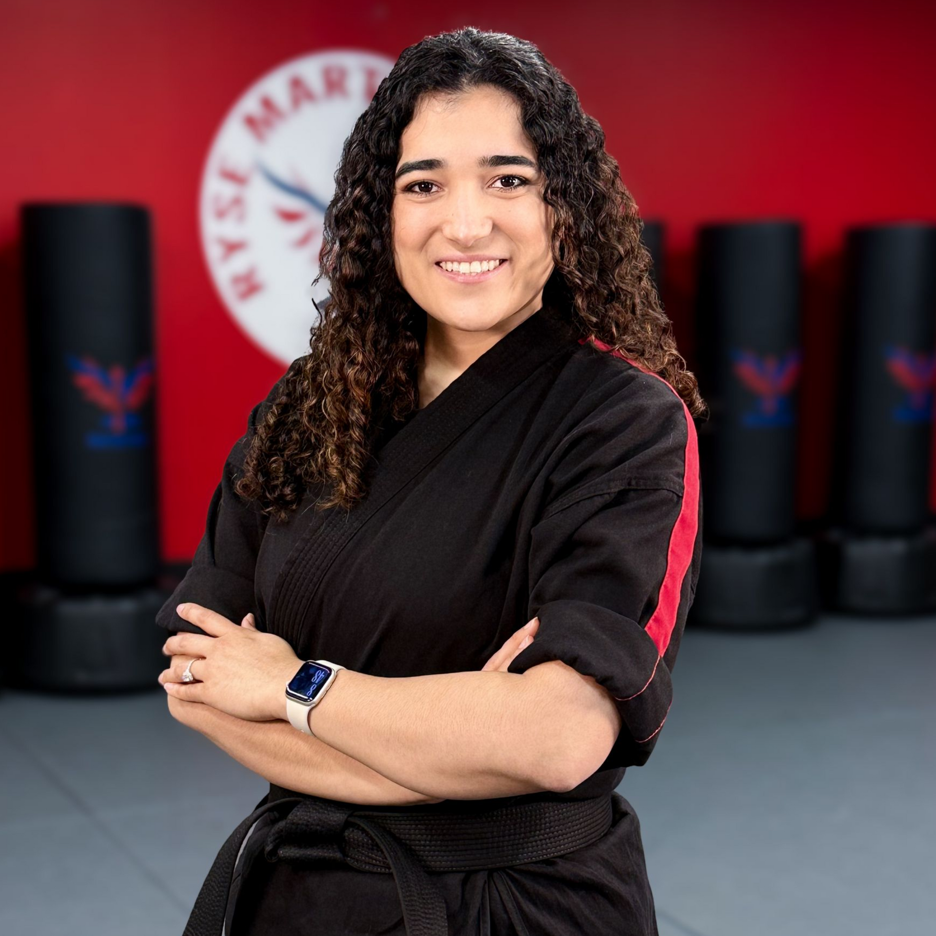 A man in a white karate uniform is standing on a blue mat in a gym.