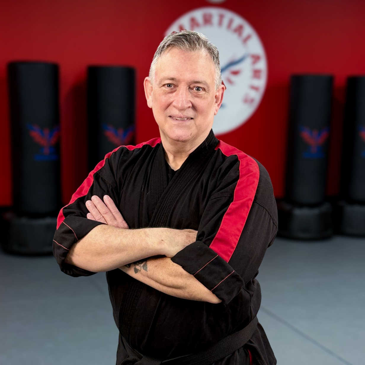 A man in a white karate uniform is standing on a blue mat in a gym.